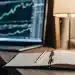 TradeAlgo complaints: Laptop with stock charts, notebook, and pen.