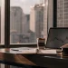 Laptop with stock chart, notebook, and coffee cup on desk.