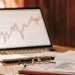 Avoid top investing mistakes. Stock chart displayed on laptop with financial documents.